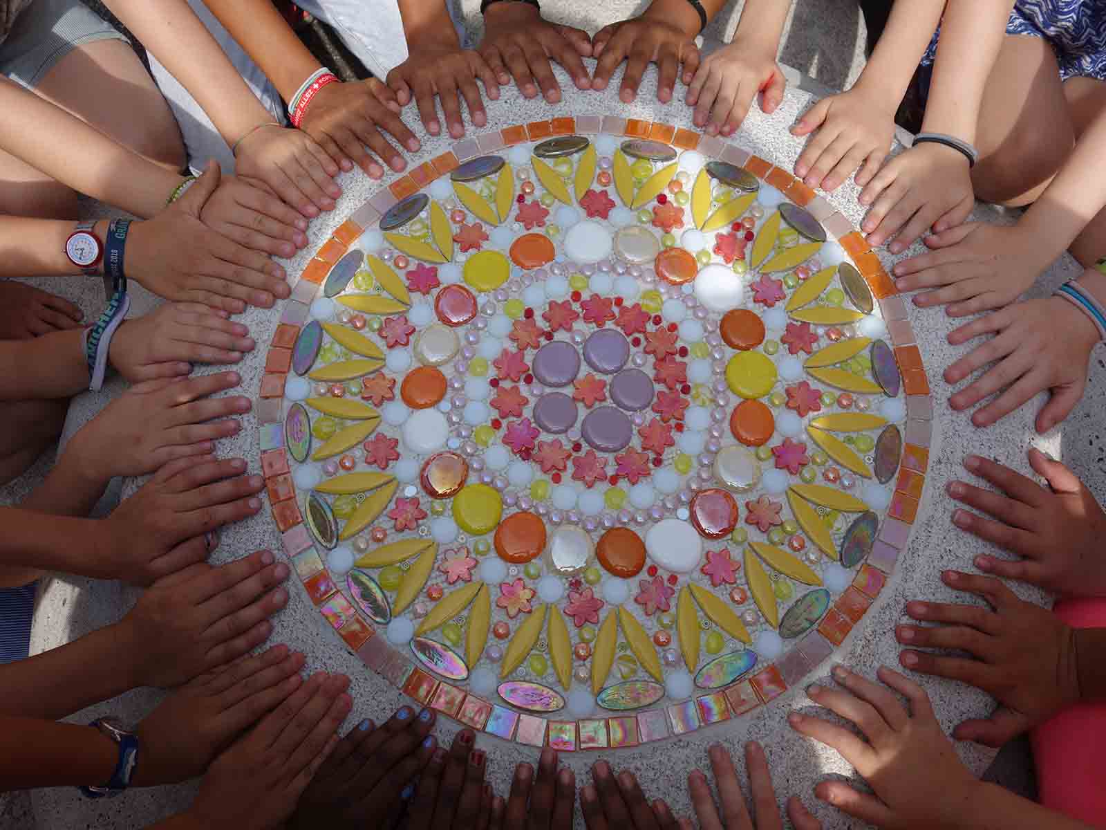 Künstlerhände um das fertige Mosaik.