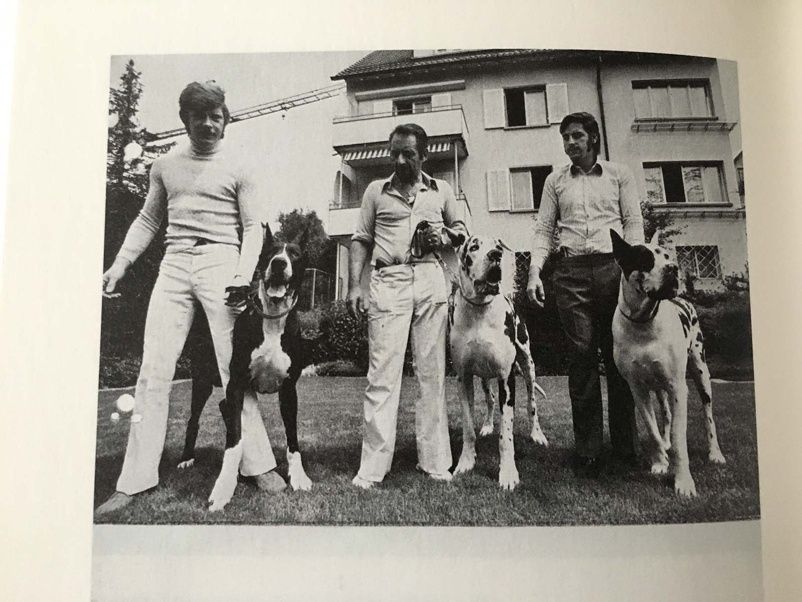 Lenzlinger und zwei Mitarbeiter präsentieren sich mit Doggen und Waffen vor dem Haus an der Ackersteinstrasse.